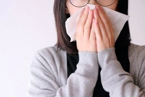花粉症で鼻をかんでいる女性の写真